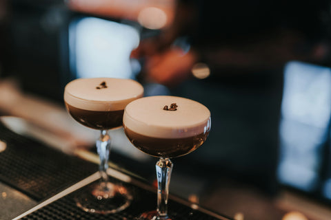 zwei Espresso Martini mit schöner Schaumkrone und Kaffeebohnen dekoriert, stehen auf einer Bar